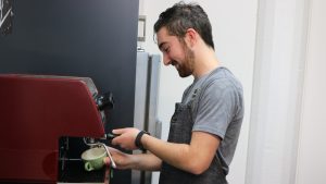 Image: A college student makes a coffee using a red coffee machine. Image provided to TASC by Don College (2019).